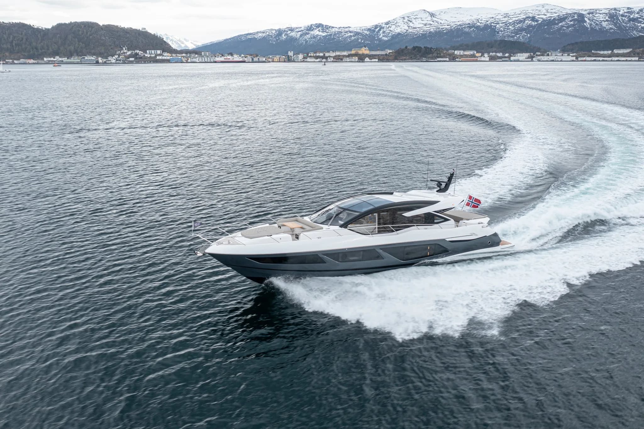 Sunseeker-yacht i sving med brespray, snødekte fjell i bakgrunnen.