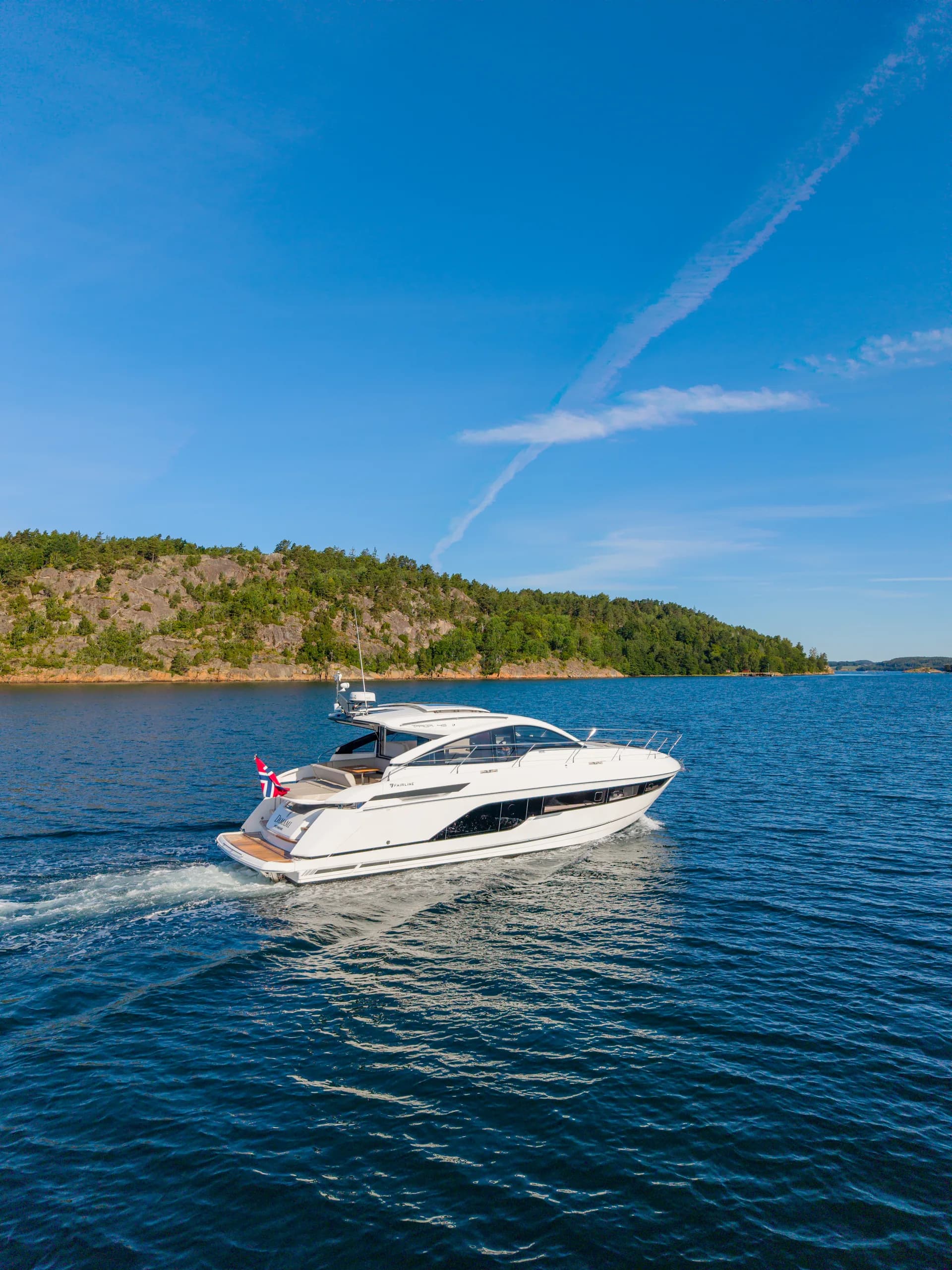 Fairline Targa 47 i fart langs klippekysten, dronebilde i portrettformat.