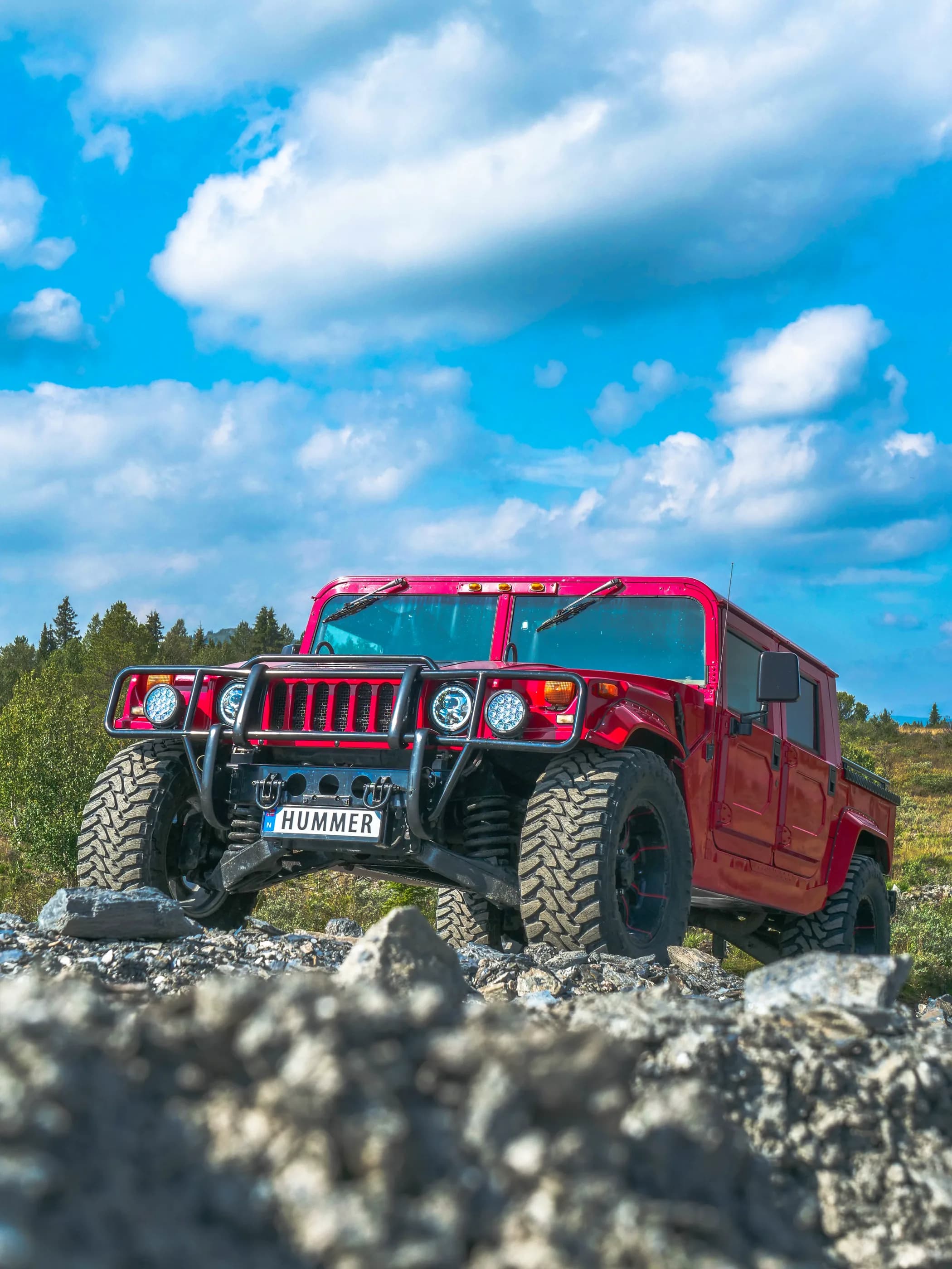 Rød Hummer H1 fotografert fra lav vinkel over grus mot blå himmel.