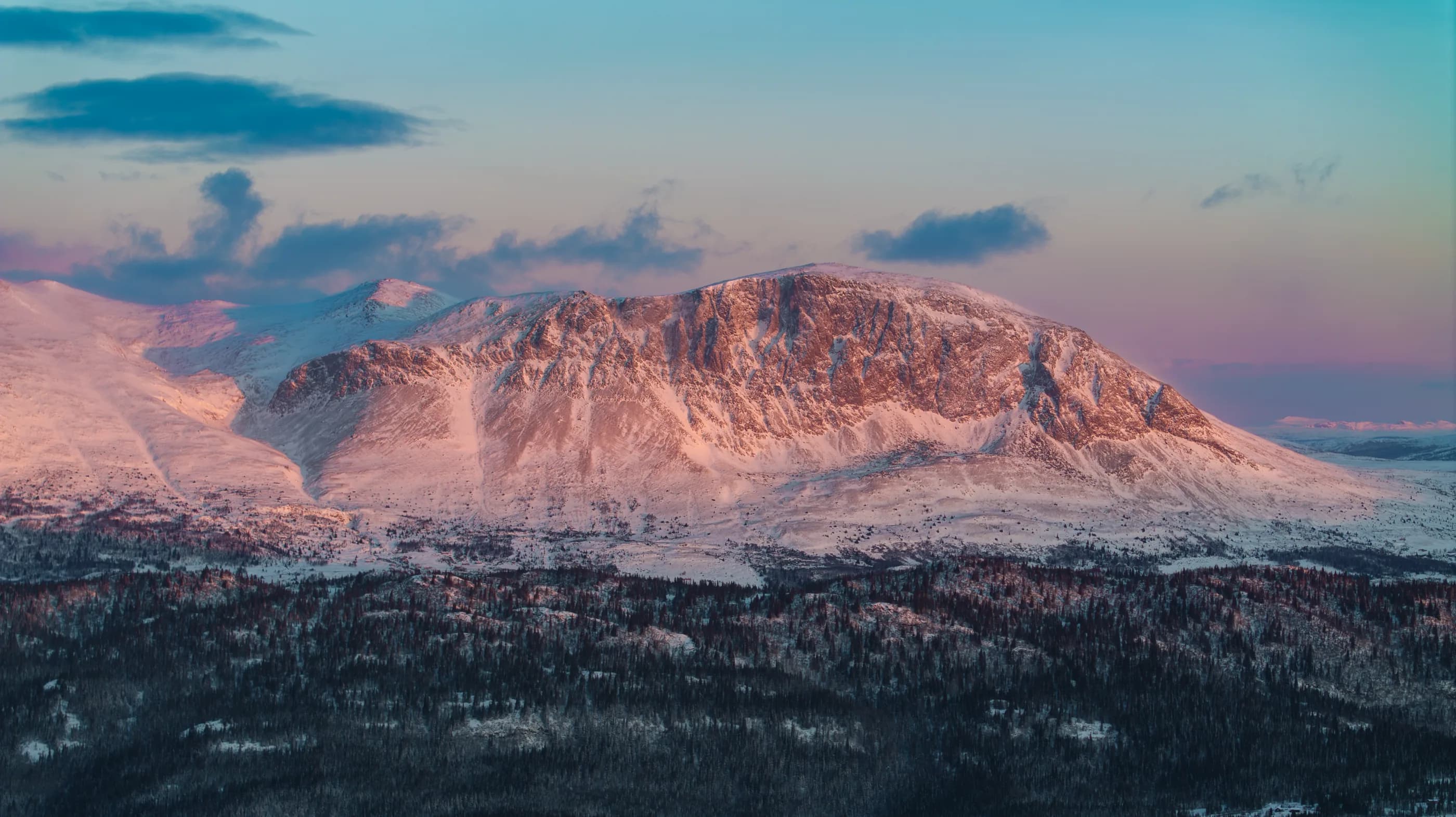 Dronebilde av et snødekt fjell i rosa solnedgangslys.