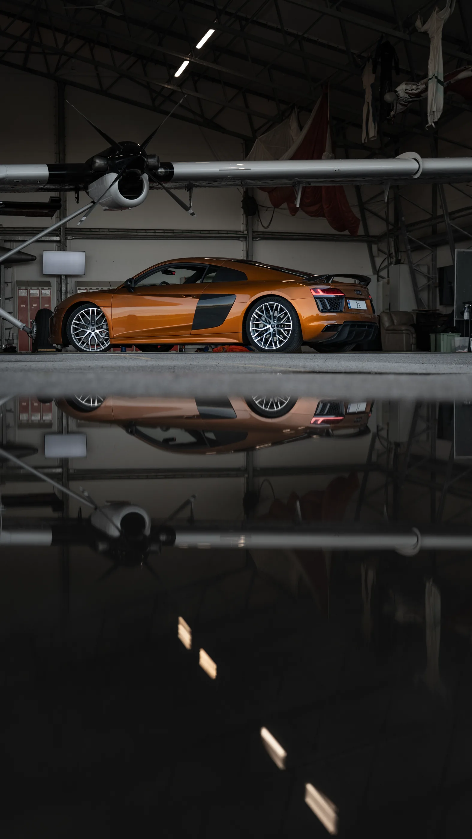 Audi R8 under vingen på et fly i hangaren, speilet i gulvet.